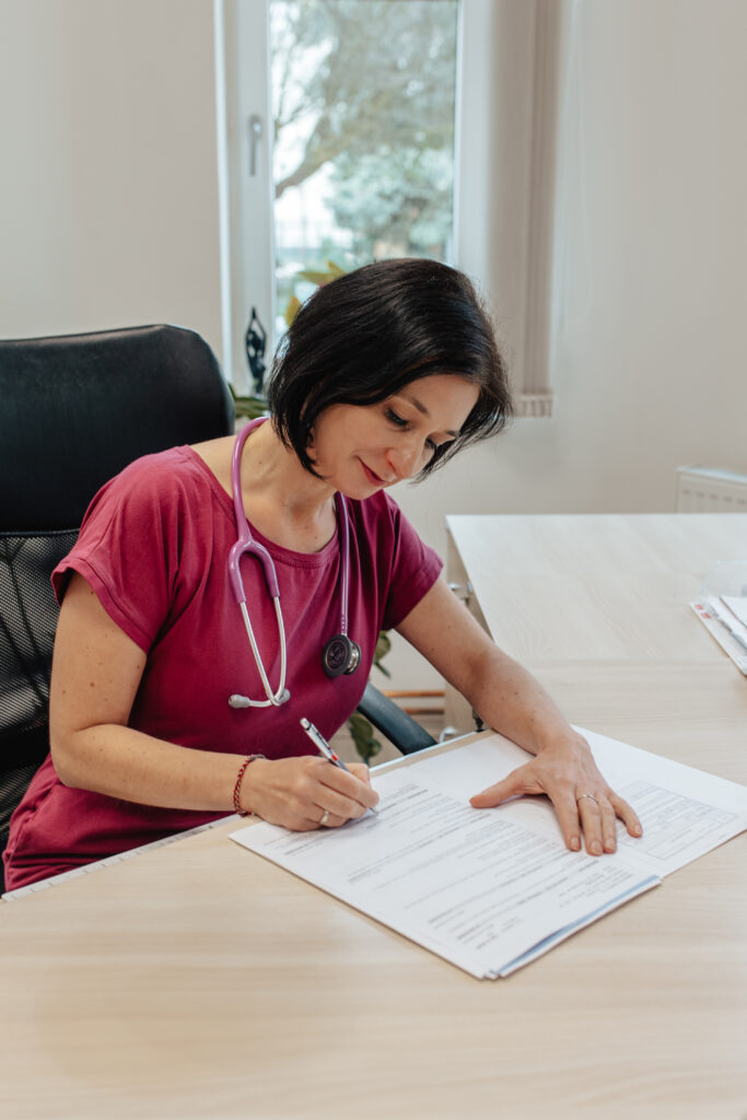 Doktorkav lékařském oděvu s fonendoskopem kolem krku píše na formulář na stole.